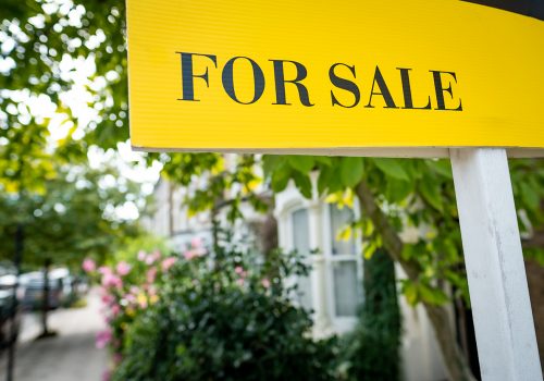 House 'For Sale' sign on suburban street of houses