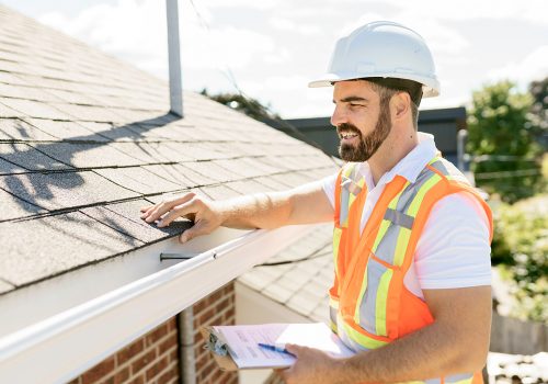 A man in a hard hat, holding a clipboard, standing on the steps of an old rundown house.