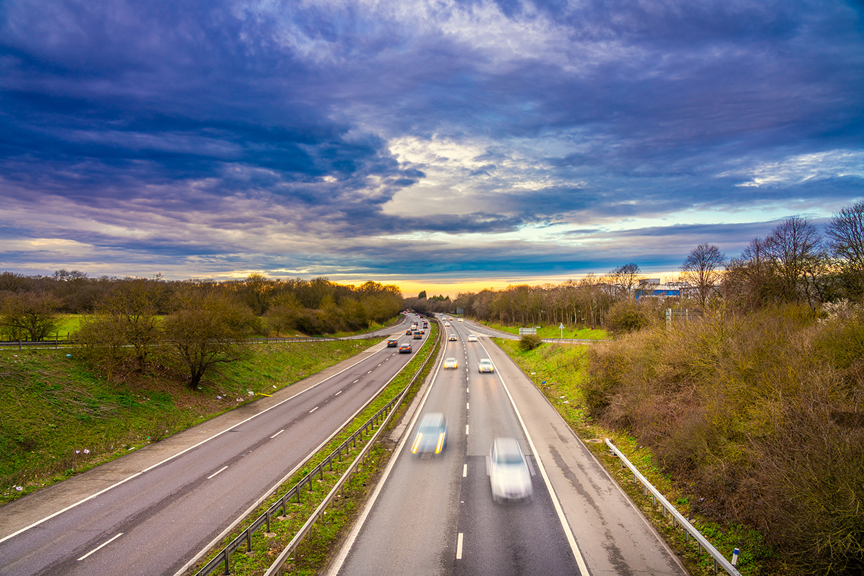 Picture of a highway with cars and blue skies with green roadside verges