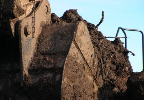 A large excavation shovel covered in mud and filled with contaminated ground waste