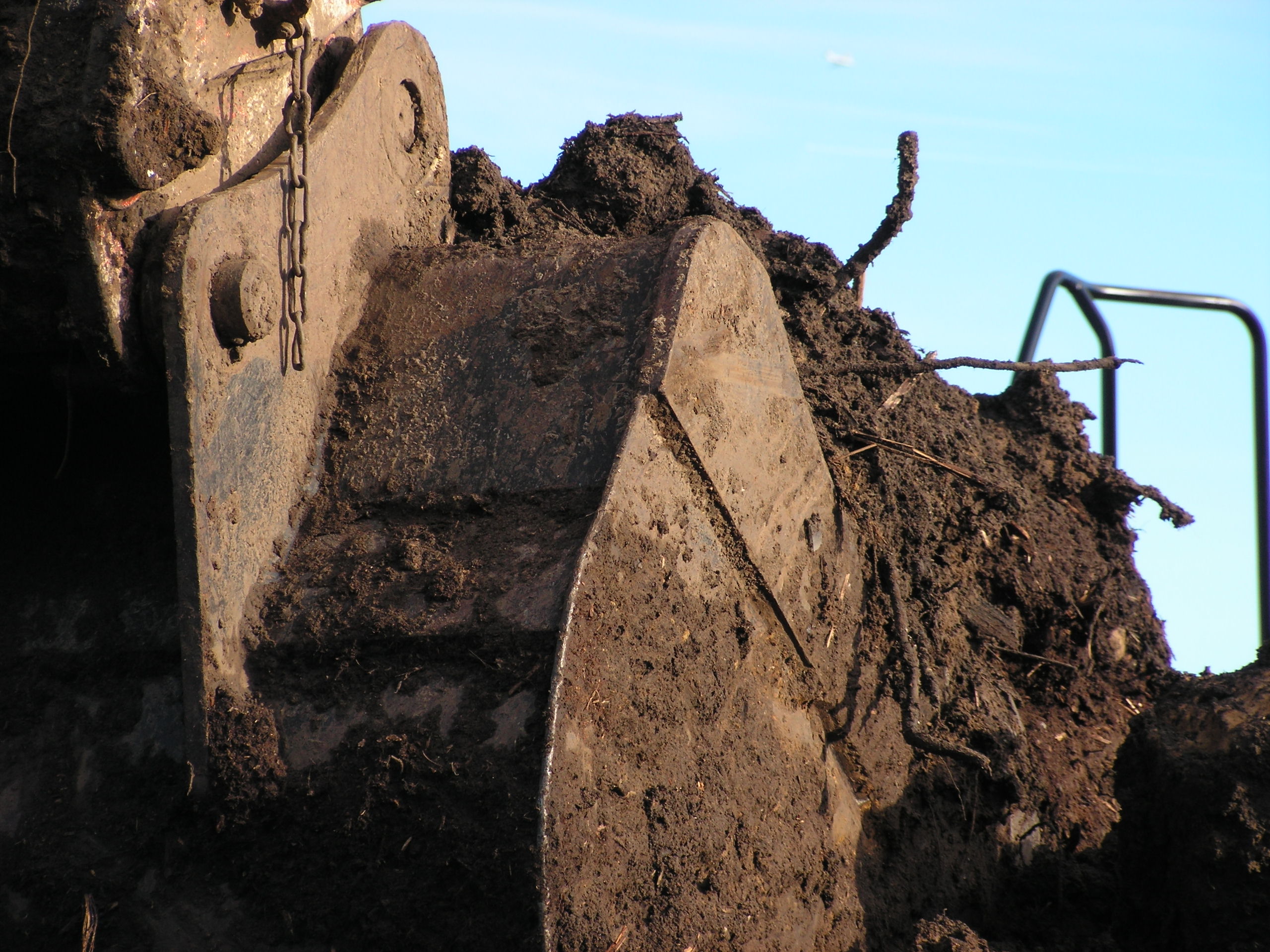 A large excavation shovel covered in mud and filled with contaminated ground waste